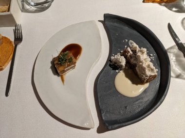 Güzel bir yemek deneyimi beyaz bir masa örtüsü üzerinde sanatsal olarak düzenlenmiş iki tabak ile sunulur..