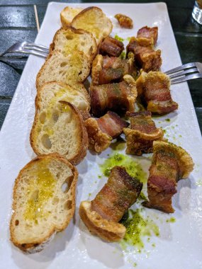 Bir tabak gevrek domuz eti ve yağlı kızarmış ekmek. Paylaşmak için mükemmel. Tabak, yeşil soslu beyaz bir tabakta servis edilir..