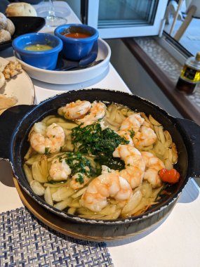 Çiğnenen lezzetli karides karidesi dökme demir bir tabakta servis ediliyor. Yanında otlar, sarımsak ve sos da var..