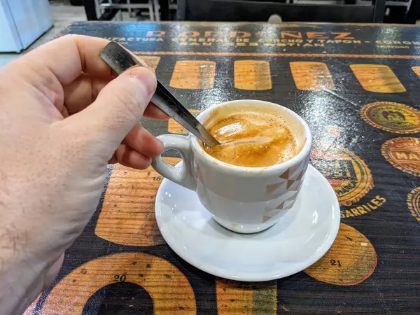 Yeni demlenmiş bir espresso 'yu beyaz bir fincanda karıştıran bir insan, sade bir ahşap masaya yerleştirilir..