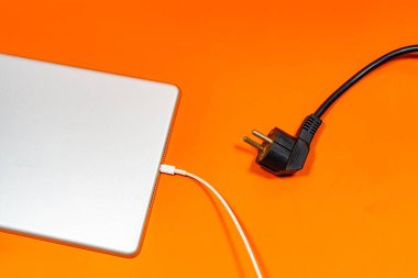 Beyaz bir kabloya bağlı gri bir tablet ve turuncu bir yüzeyde siyah bir kablo.. 