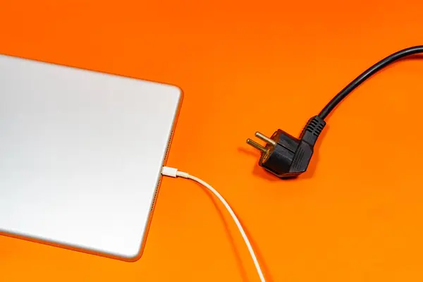 Beyaz bir kabloya bağlı gri bir tablet ve turuncu bir yüzeyde siyah bir kablo.. 