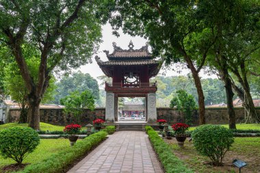 Manzaralı bir yol, Hanoi, Vietnam 'da ünlü bir simge olan Edebiyat Tapınağı' nın antik bir kapısına çıkıyor. Yeşiller yemyeşil ve ağaçlar tarihi mekanı sarmış durumda..