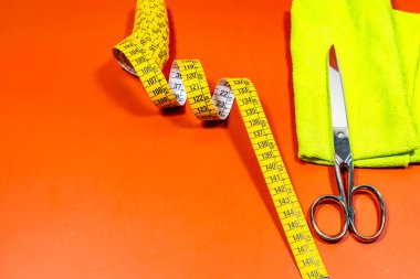 Bir mezura ve makas, turuncu bir masanın üzerinde sarı bir bez ile..