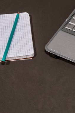 Not defteri, kalem ve dizüstü bilgisayar kahverengi bir yüzeye yerleştirilerek çalışma alanı veya çalışma ortamı oluşturulur.