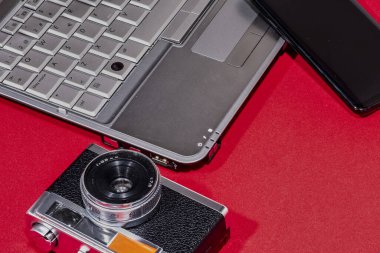 Bir dizüstü bilgisayar, klasik kamera ve cep telefonu, çağlar boyunca kullanılan teknolojiyi gösteren kırmızı bir yüzeye yerleştirilmiştir..