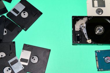 Disketlerin ve sabit disklerin bir koleksiyonu, farklı teknolojik dönemlerin kalıntıları, bir turkuaz arka planda karşıtlık