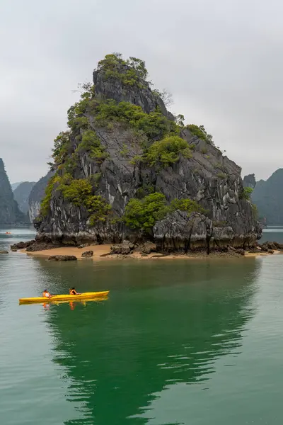 Sarı bir kano, Vietnam 'daki Ha Long Körfezi' nin sakin sularında süzülüyor. Yeşilliklerle kaplı görkemli bir adanın yakınında..