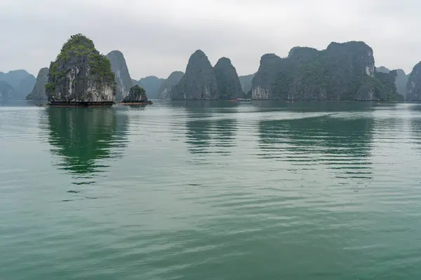 Vietnam 'da bulutlu bir gökyüzünün altında sudan yükselen kireçtaşı karistiyle simgesel Ha Long Körfezi' nin huzurlu manzarası..