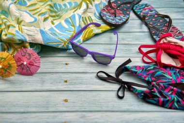 Mayo, güneş gözlüğü, terlik ve ahşap bir masanın üzerinde tropik bir iz olan plaj havlusu..