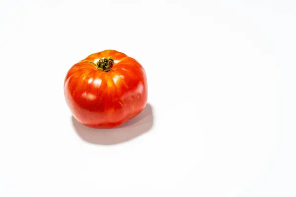 Canlı, olgun bir domates, parlak beyaz bir zemin üzerinde oturur, zengin rengi çarpıcı bir kontrasttır.
