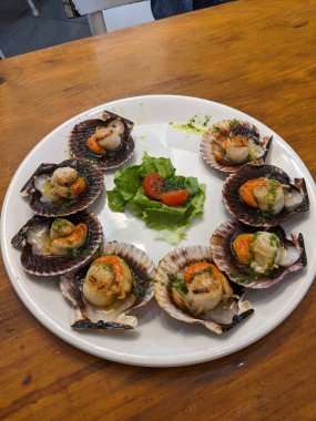 Taze domateslerle servis edilen ve otlarla süslenmiş güzel bir tabak deniz tarağı. Tadını çıkarmaya hazır..