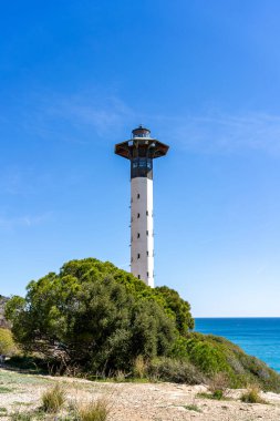 Altafulla, Tarragona 'da yemyeşil bitki örtüsü ve açık mavi Akdeniz ile kıyı uçurumunda uzun bir deniz feneri duruyor..