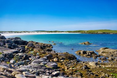 İrlanda 'da berrak mavi bir gökyüzünün altında turkuaz su ve kayaların olduğu çarpıcı bir sahil manzarası..