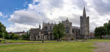 Dublin, İrlanda 'da yemyeşil çimlerle bezenmiş tarihi bir katedralin panoramik görüntüsü..
