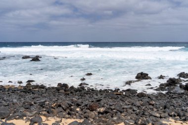 Lanzarote, La Graciosa 'nın engebeli kıyı şeridi, dalgalar sahildeki volkanik kayalara çarpıyor..