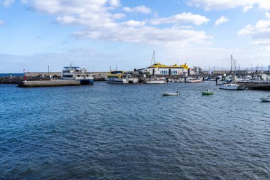 A vibrant harbor scene in Lanzarote showcases ferries, boats, and yachts against a bright, cloud-streaked sky, and a sea view. Lanzarote, Spain, 2025-07-20