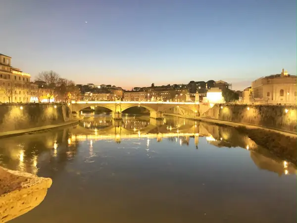  Roma 'daki Tiber Nehri' nin sakin bir manzarası, alacakaranlıkta, şehir ışıklarının sıcacık parıltısıyla aydınlanıyor.
