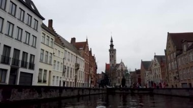 Belçika 'nın tarihi Bruges şehrinde manzaralı bir kanal manzarası. Brüj 'ün ikonik çan kulesi kanalı kaplayan renkli binaların üzerinde..