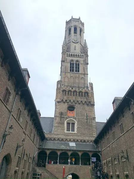 Bruges 'ün çan kulesinin bir fotoğrafı, şehrin merkezinde uzun, Gotik bir kule. Kule tarihi binalar ve kaldırım taşlı caddelerle çevrili..