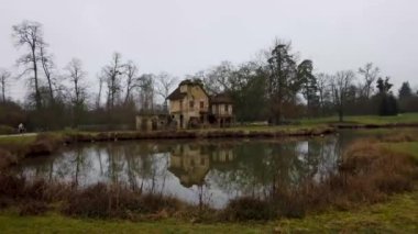 Fransa 'nın Versailles Sarayı' ndaki Queens Hamlet Le Hameau de la Reine manzarası sakin bir gölete yansıyan resimli bir kır evi..