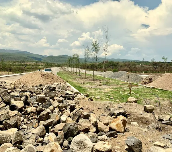  Etrafı kayalık arazilerle çevrili, yeni döşenmiş bir yol ve kabarık bulutlu açık mavi gökyüzü olan bir inşaat alanı..
