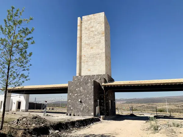 Leon, Guanajuato 'daki modern bir mimari girişin fotoğrafı. Taştan yapılmış uzun, dikdörtgen bir kule ve bir yola bağlanan köprü benzeri bir yapı içeriyor..