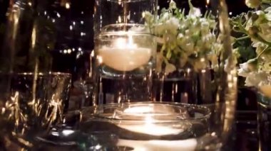 Büyüleyici yakın plan bir düğün süsü içinde cam bir vazoda yüzen bir mum, narin beyaz çiçekler ve parıldayan ışıklarla çevrili. 