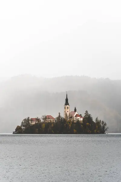 Slovenya 'nın Bled Gölü adasındaki ikonik şapelin panoramik görüntüsü. Zümrüt suları ve görkemli bir dağ zeminiyle çevrili..