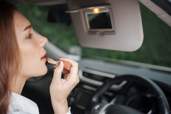 Женщина использует зеркало заднего вида для нанесения макияжа во время вождения своей машины
.