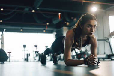 Spor salonunda egzersiz yaparken tahta egzersizi yapan genç bir kadın..