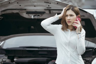 Yoldaki bozuk arabanın yanında genç bir kadın acil yardım çağrısı yapıyor..