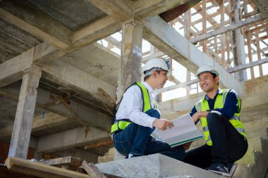 Asian Architector and engineers team with draft plan of building and  talking constructing site. Construction manager and engineer working on building site.