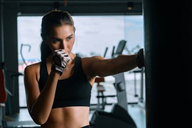 Young woman practicing boxing at the gym, she wears boxing gloves and hits a punching bag.