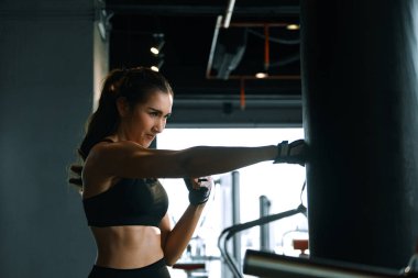 Young woman practicing boxing at the gym, she wears boxing gloves and hits a punching bag.