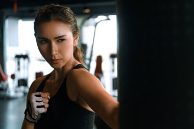Young woman practicing boxing at the gym, she wears boxing gloves and hits a punching bag.