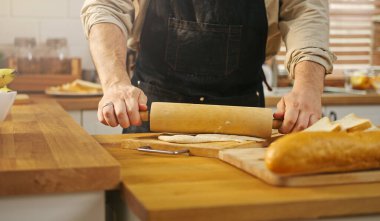 Yakından bakan adam önlük takıyor, elinde oklavayla mutfak masasında para kazanıyor..