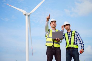 İki Asyalı mühendis rüzgar türbini çiftliğinde türbinleri tartışıp kontrol ediyorlar. Yenilenebilir enerji teknolojisi ve sürdürülebilirlik.