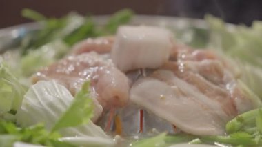 Grilled pork on the stove, Thai food buffet. Hands holding chopsticks grilling traditional Thai style BBQ with pork, prawns, beef, chicken, vegetables and soup on hot pan.