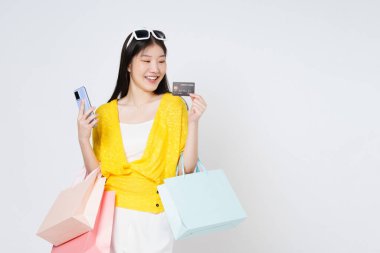 Kredi kartı ve cep telefonu kullanan, beyaz arka planda izole edilmiş alışveriş torbaları taşıyan mutlu genç bir kadın..