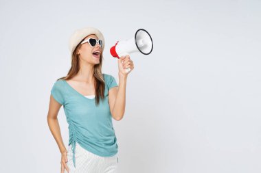 Güneş şapkası takan, güneş gözlüğü takan ve elinde megafon tutan genç bir kadın. Yaşam tarzı yaz ve duyuru konsepti.