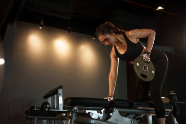 Spor salonunda ağırlık plakasıyla egzersiz yapan sporcu bir kadın..