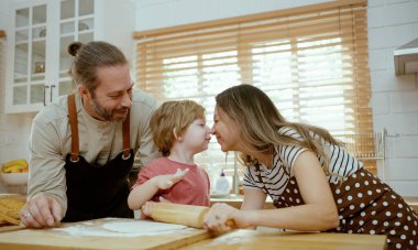 Baba ve anne, bebek oğluna evde mutfak tezgahında hamur yoğurmayı öğretiyor. Ebeveynler ve çocuklar birlikte yemek pişirmekten zevk alır ve eğlenirler..