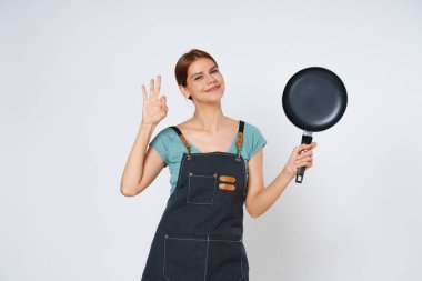 Restoran sahibi kadın tamam işareti gösteriyor ve tavayı beyaz arka planda tutuyor..