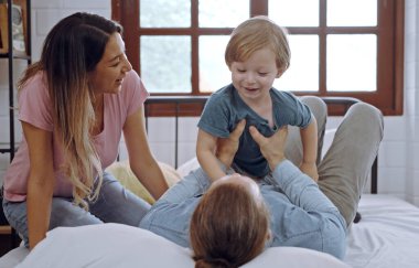 Mutlu aile, anne, baba ve oğul gülüyor, yatak odasında oynuyorlar..