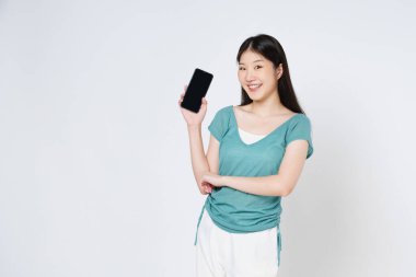 Elinde cep telefonu olan gülümseyen Asyalı kadın beyaz arka planda tek başına dikiliyordu..