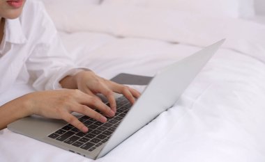 Genç Asyalı kadın yatak odasında dizüstü bilgisayar kullanıyor ve daktilo kullanıyor..