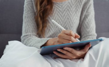 Kanepede oturan Asyalı genç kadın dijital tablet ve kalem kullanarak alışveriş yapıyor ya da evde internet üzerinden çalışıyor..