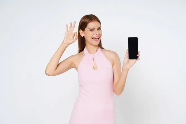 Ung Kvinna Som Håller Smartphone Och Visar Tecken Vit Bakgrund Royaltyfria Stockbilder