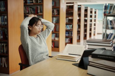 Asyalı öğrenci kadın üniversitede kütüphanede kitap okuyordu. Genç kız yorgunluğu sıkı çalışırken sorun yaşıyor. Üzüntü konsepti